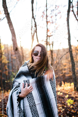 Girl bundled up with a blanket in a woods at sunset in the fall