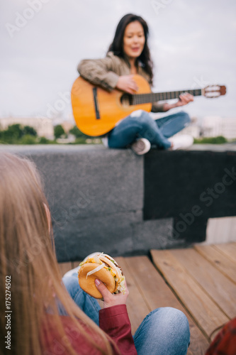 Music junkie with junk food on live show. Girl with fastfood in hands listen singer's acoustic guitar improvisation. photo