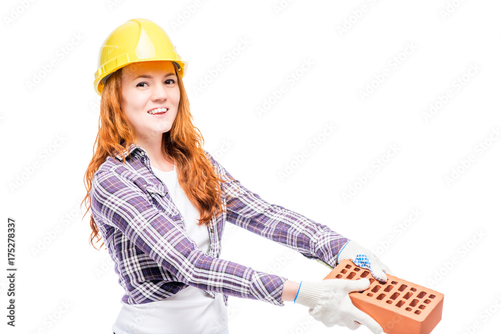 beautiful woman with red hair holds a brick, wearing a yellow helmet on her head beautiful woman with red hair holds a brick, wearing a yellow helmet on her head