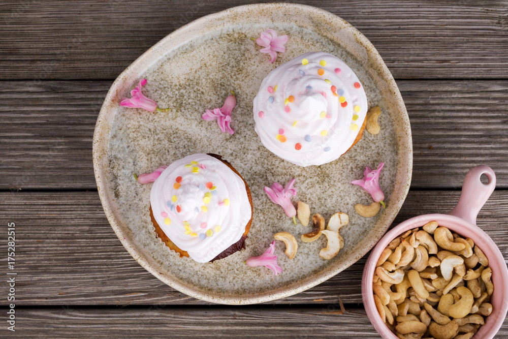 Two beautiful cupcakes served on wooden table decorated with cashews and small pink flowers