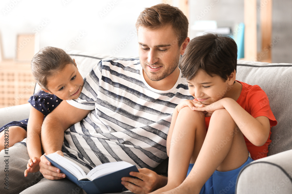 Young man and his little children reading book at home Young man and his little children reading book at home