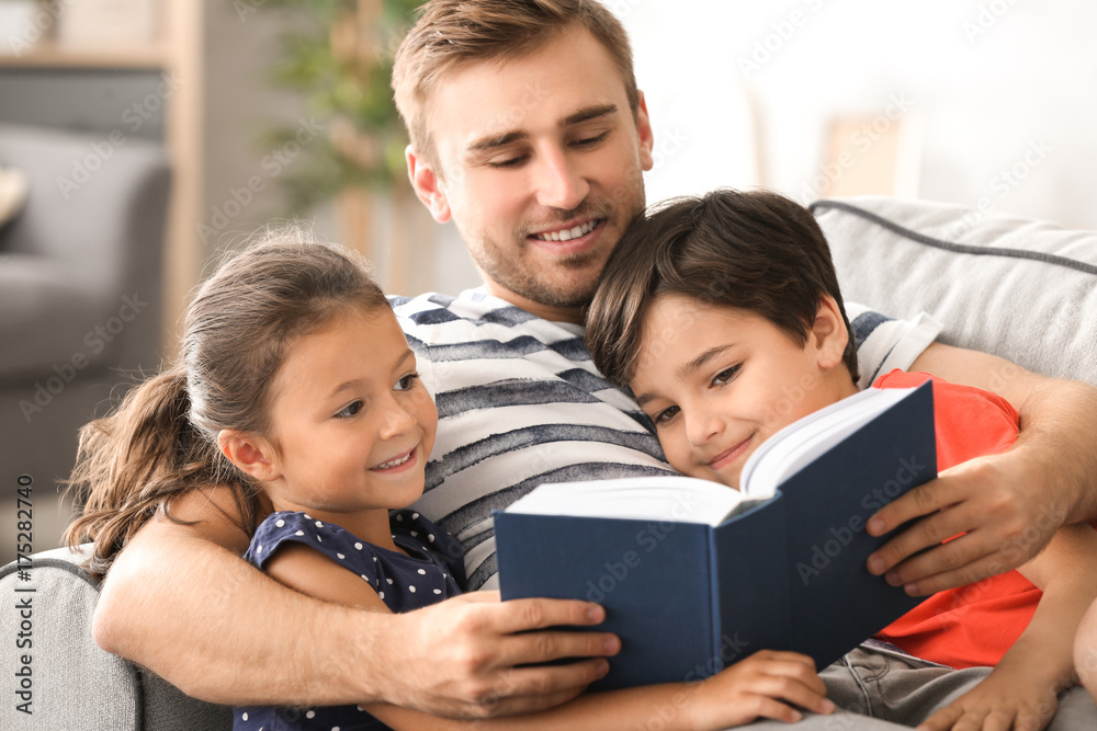 Young man and his little children reading book at home Young man and his little children reading book at home