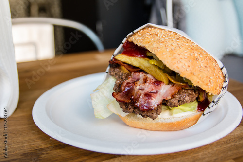 Smaczny Burger wołowy na białym talerzyku owinięty w papierem - bekon i warzywa  photo