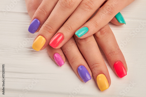 Multicolored manicure close up. Young woman hands with pastel manicure on white wooden background. Summer fashion manicure.