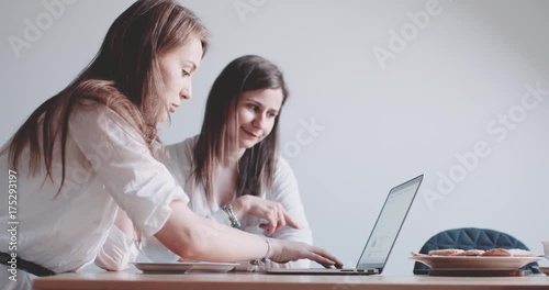 Two Women working on Laptop, searching internet. Slow Motion 120 fps 4K DCi. Friends sharing coffee using computer. Young women shopping online together, having tea and conversation at home.