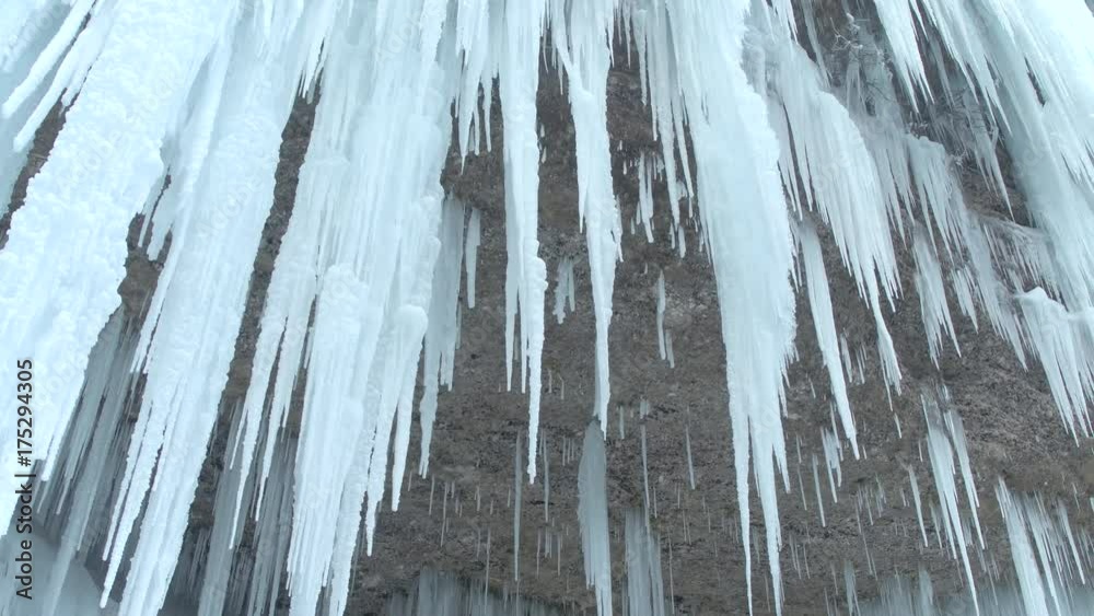 CLOSE UP Stunning frozen waterfall icicles on rocky mountain cliff on winter day. Winter cascade frozen into numerous white icicles. Waterfall falling past hundreds of icicles Fantastic winter scenery CLOSE UP Stunning frozen waterfall icicles on rocky mountain cliff on winter day. Winter cascade frozen into numerous white icicles. Waterfall falling past hundreds of icicles Fantastic winter scenery