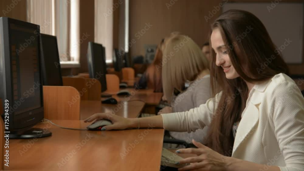 Business woman working on the computer. A group of young people in a computer classroom. Young brunette woman smiling Business woman working on the computer. A group of young people in a computer classroom. Young brunette woman smiling
