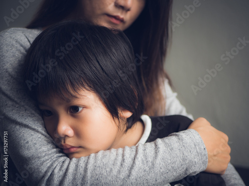 Closeup sad little boy being hugged by his mother at home. Parenthood, Love and togetherness concept.