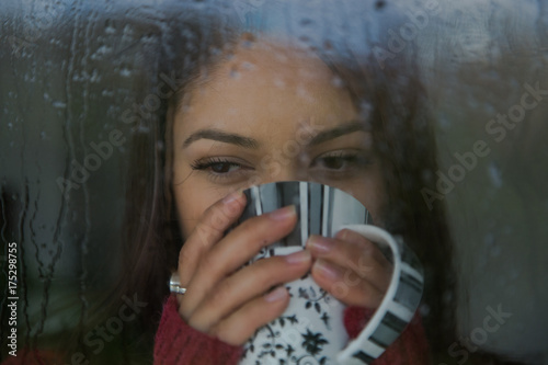 Beautiful woman is looking through the window on a rainy day.