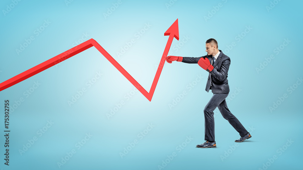 A businessman in red boxing gloves punches a red statistic arrowed line to make it raise up. A businessman in red boxing gloves punches a red statistic arrowed line to make it raise up.