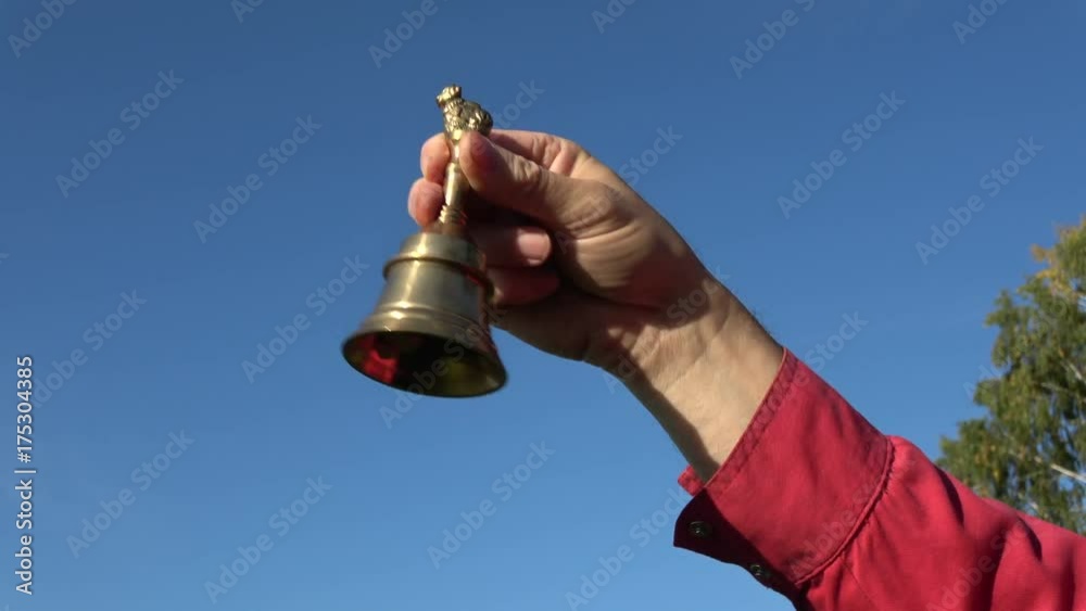 Man hand ringing brass bell on sky background and beautiful sound

