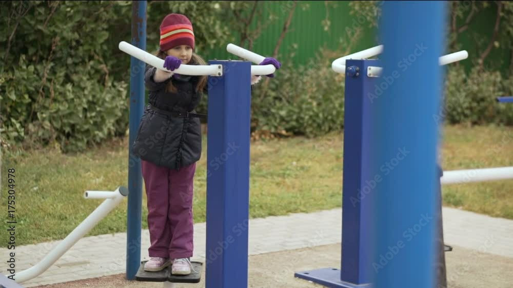 Little cute girl is engaged on the simulator for training of waist muscles on the sportsground in the autumn time. Slow motion. Little cute girl is engaged on the simulator for training of waist muscles on the sportsground in the autumn time. Slow motion.