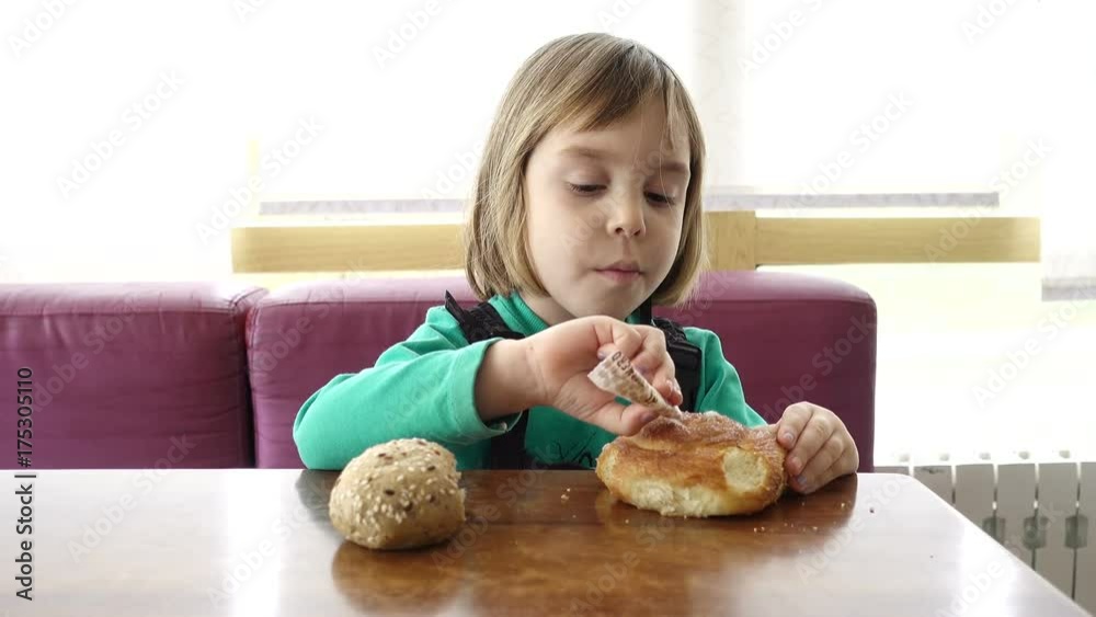 A European girl is sitting in the kitchen, looking attentively at the TV and eating a sweet bun. A European girl is sitting in the kitchen, looking attentively at the TV and eating a sweet bun.