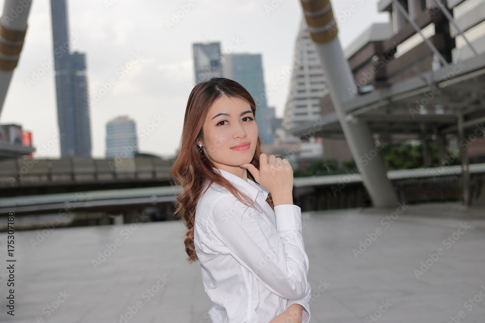 Portrait of confident young Asian woman with white shirt looking on camera at urban building public background.