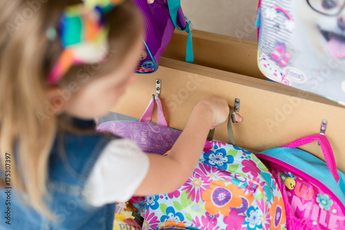 A young girl is hanging her backpack on her first day of school.