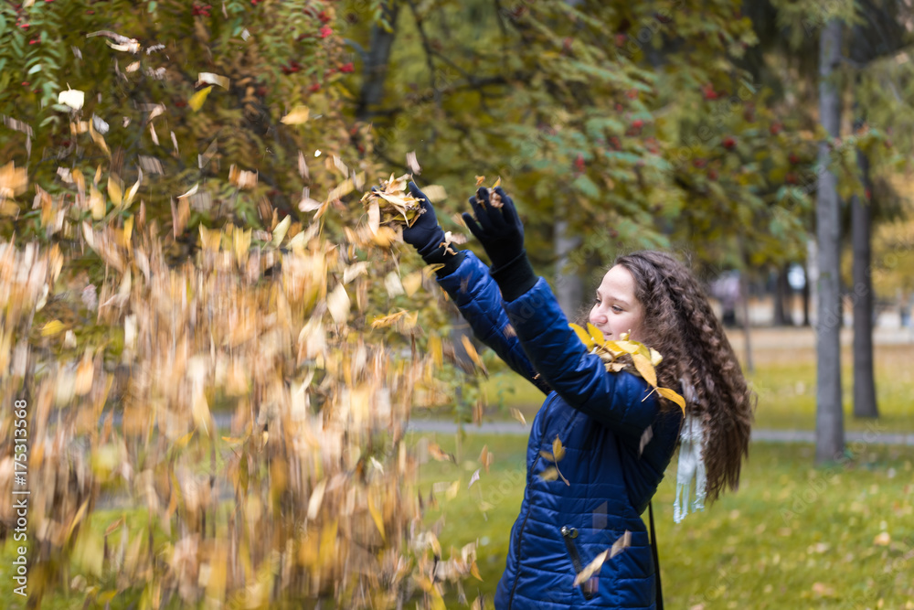 A girl with curly hair throws autumn leaves