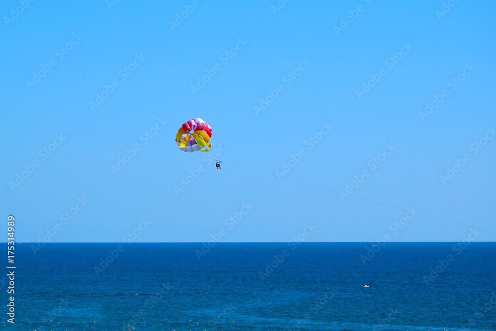 Tourists fly over the sea on a parachute behind a boat (Paraseyling).
