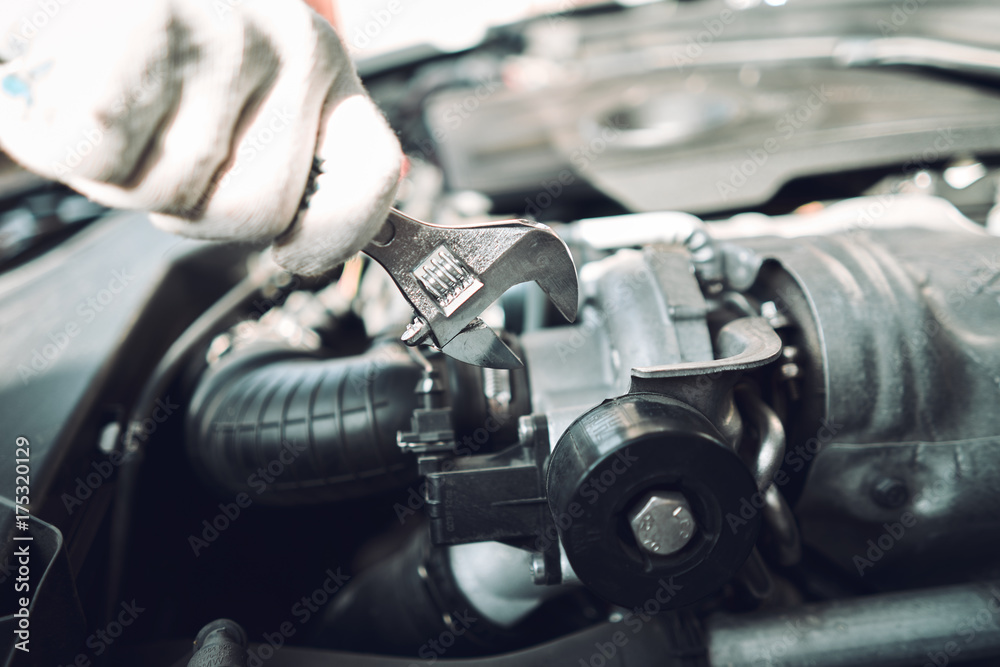 Close-up. The auto mechanic is fixing a car with a wrench. White car. White gloves for repair