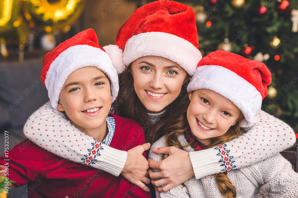 mother embracing with kids in santa hats mother embracing with kids in santa hats
