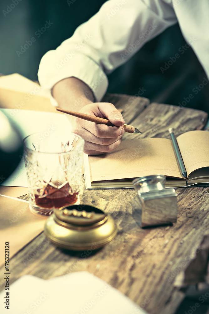 Writer at work. Handsome young writer sitting at the table and writing something in his sketchpad Writer at work. Handsome young writer sitting at the table and writing something in his sketchpad