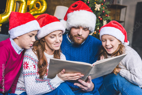 family in santa hats reading book