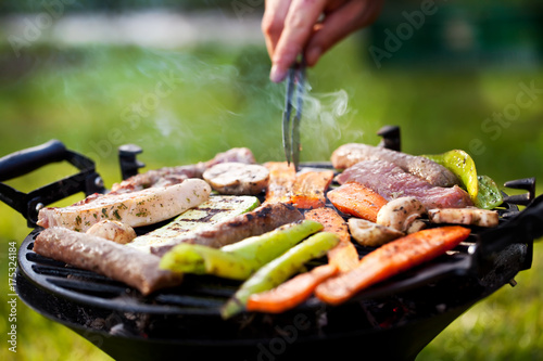Photography Horizontal close-up of a woman's hands over a hot and smokey grill, where different animal products and scallions or green onions are slowly roasting
