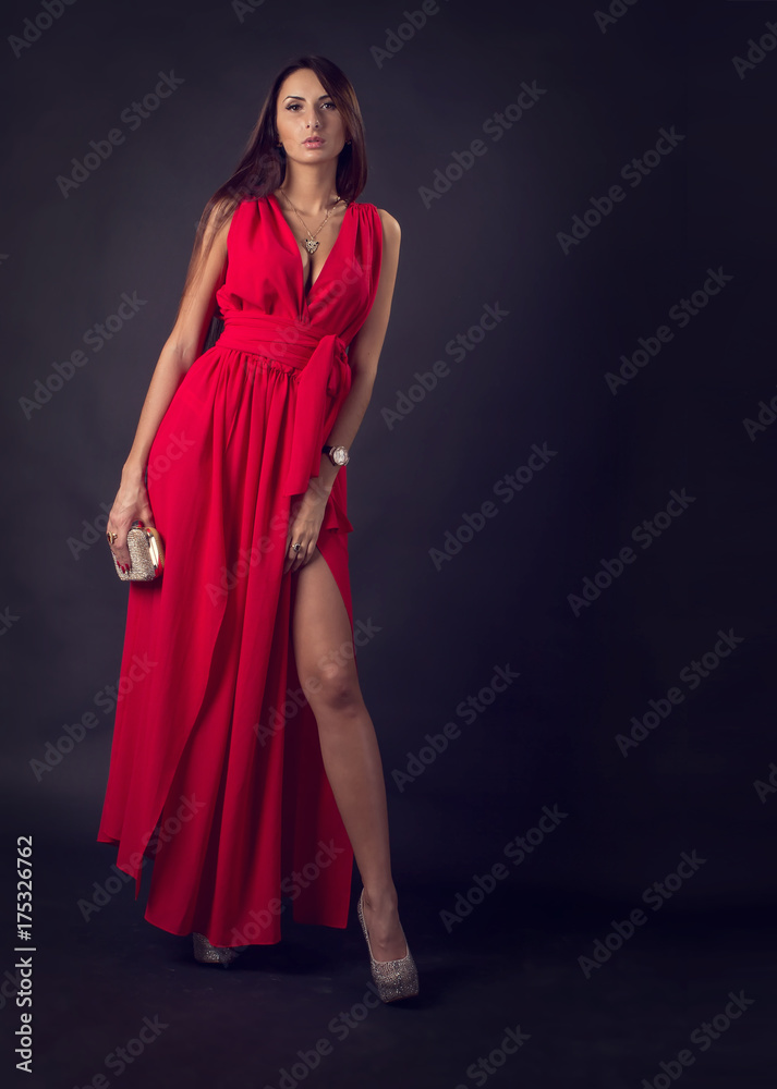 Fototapeta premium Sensual elegant young woman in red dress. Glamour woman. Modern woman in an evening cocktail red dress on a dark background. Party.