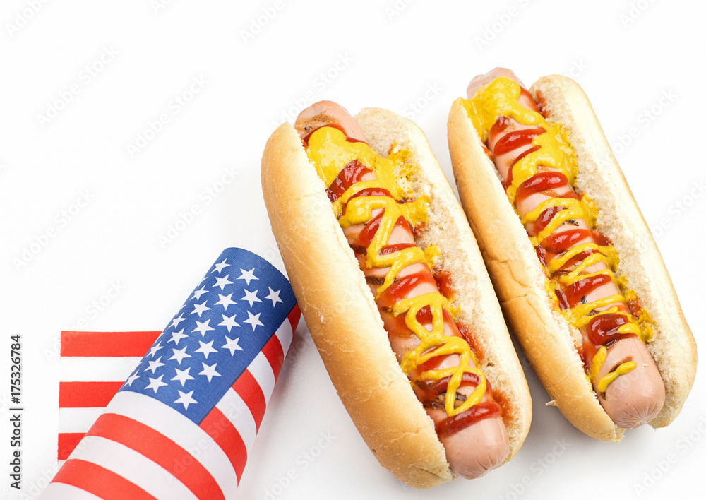 Two hotdogs with ketchup and mustard next to American flag on white background. Isolated. Fastfood. Two hotdogs with ketchup and mustard next to American flag on white background. Isolated. Fastfood.
