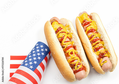 Fototapeta Naklejka Na Ścianę i Meble -  Two hotdogs with ketchup and mustard next to American flag on white background. Isolated. Fastfood.