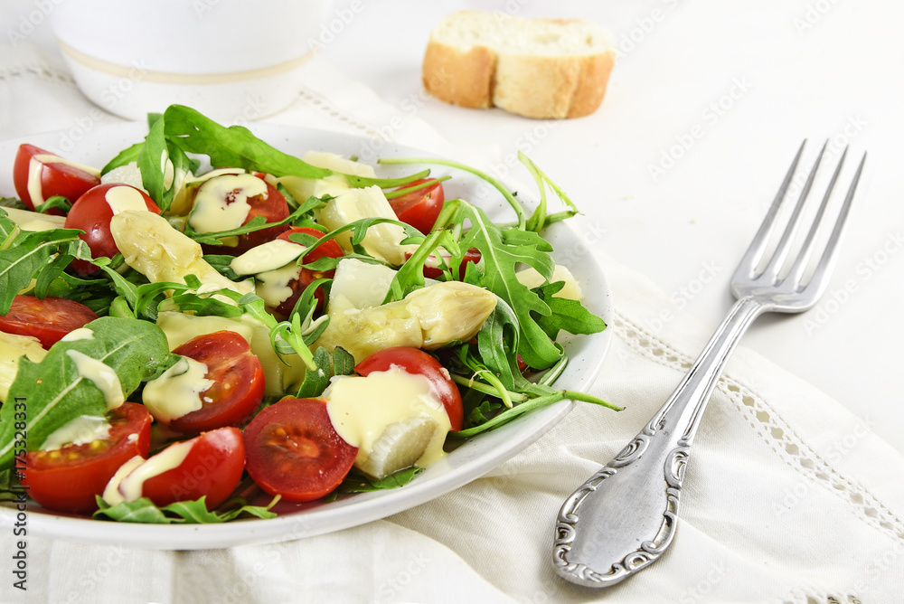 mixed salad of white asparagus, cocktail tomatoes and arugula healthy snack with a fork on a bright background, copy space, close up