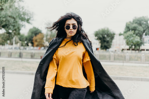 Portrait of stylish modern young curly woman in coat sunglasses. She on the street and looks happy. Truly emotions. photo