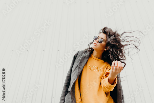 Portrait of stylish modern young curly woman in coat sunglasses. She smile at camera on the street and looks happy. Truly emotions. photo