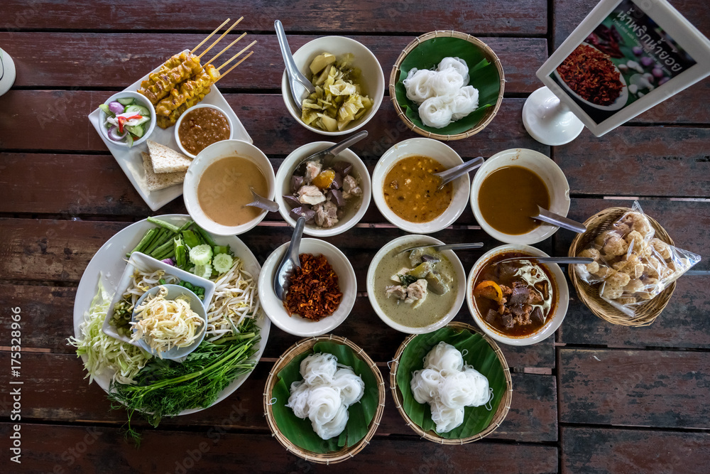 Thai food on the old wooden table Include Pork satay, Thai Green Curry, Spicy pork sauce (Thai language Nam Ngeaw), Pickled Lettuce, Crispy pork skin, Fresh vegetable and Boil the pork.