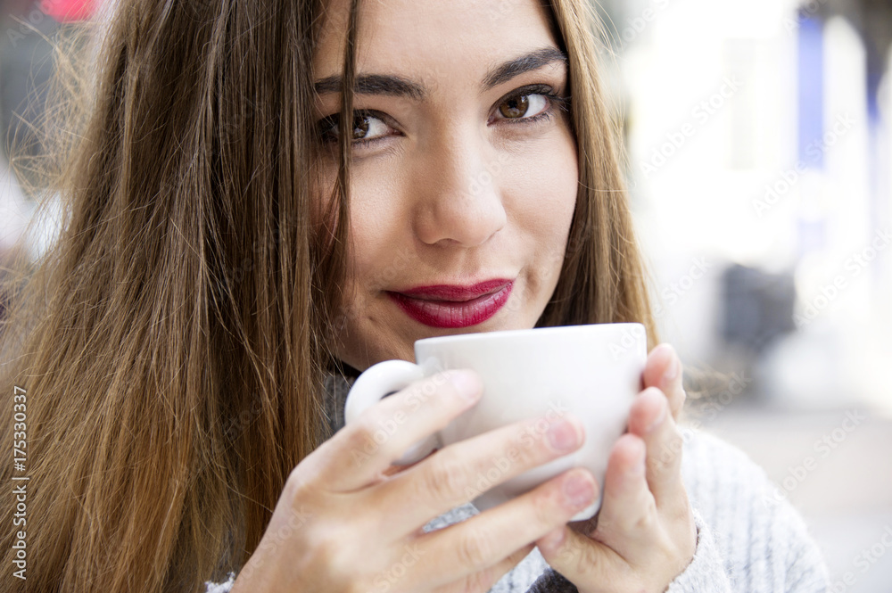 Attractive young woman is having a coffee on a street with street life background in autumn time. Lifestyle concept. Attractive young woman is having a coffee on a street with street life background in autumn time. Lifestyle concept.