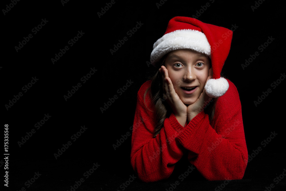 Merry Christmas. The young girl in a red sweater and Santa's hat looks at the viewer and enjoys. Merry Christmas. The young girl in a red sweater and Santa's hat looks at the viewer and enjoys.
