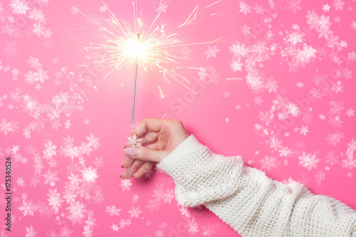 Sparkling Bengal fire in a woman's hand on a pink background. Christmas Concept