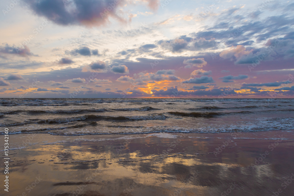 A pink, blue and purple creamy cloudy sunset, with sun rays breaking through the clouds. A relaxed quiet sunset evening on the coast.