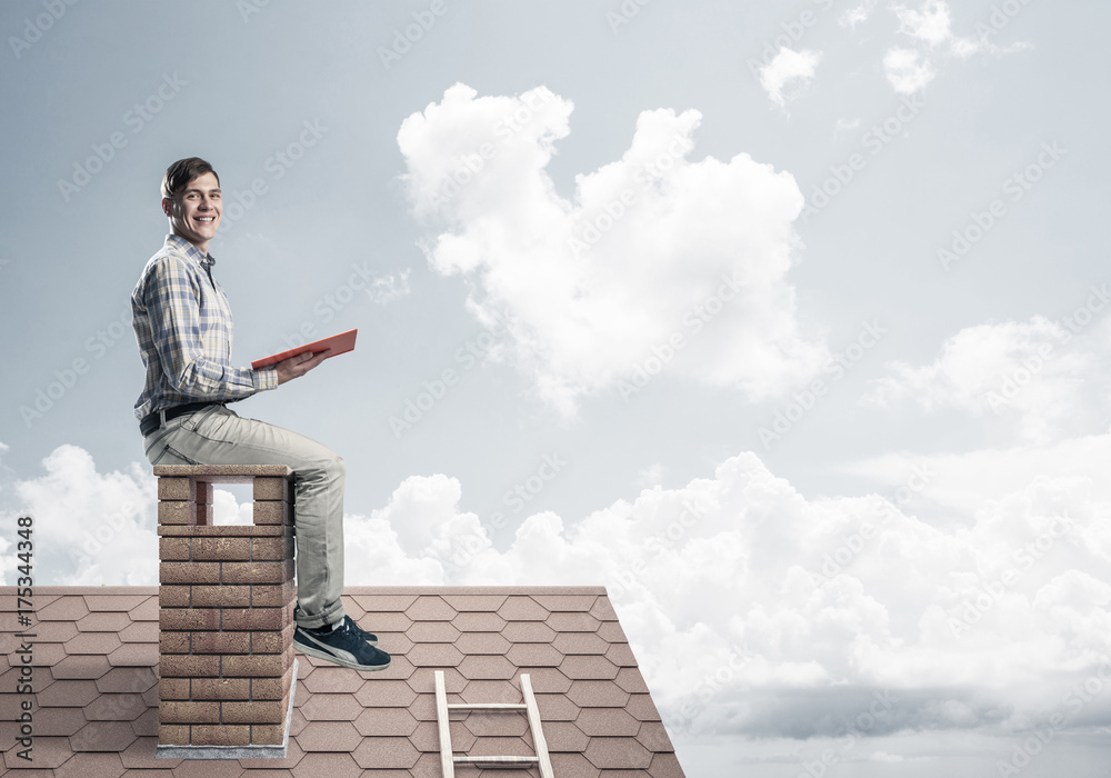 Handsome man on brick roof against cloud scape reading book Handsome man on brick roof against cloud scape reading book