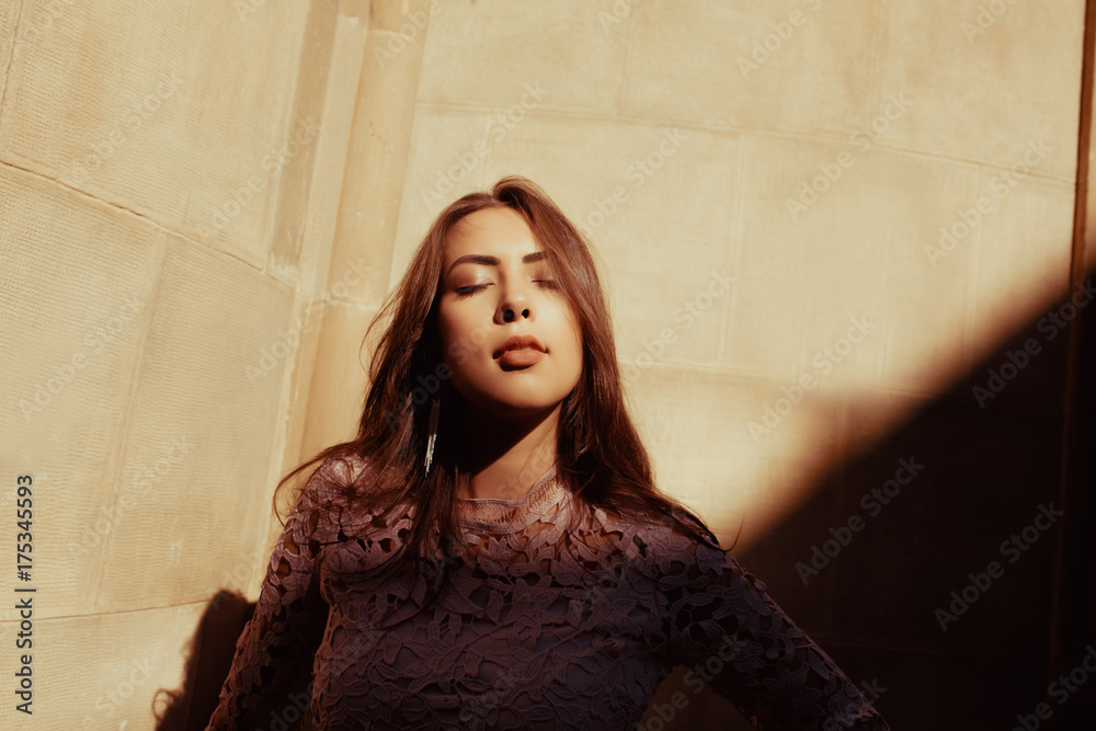 Fototapeta premium Sensual brunette model with closed eyes posing at the courtyard with shadow on her face