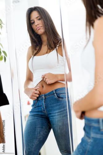 Beautiful young woman looking herself reflection in mirror at home.