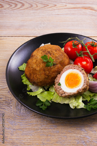 Scotch eggs on a plate with cherry tomatoes and salad, vertical