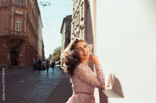 Gorgeous young model with beautiful smile posing at the street in sunny day. Woman wearing fashionable lace dress © vpavlyuk
