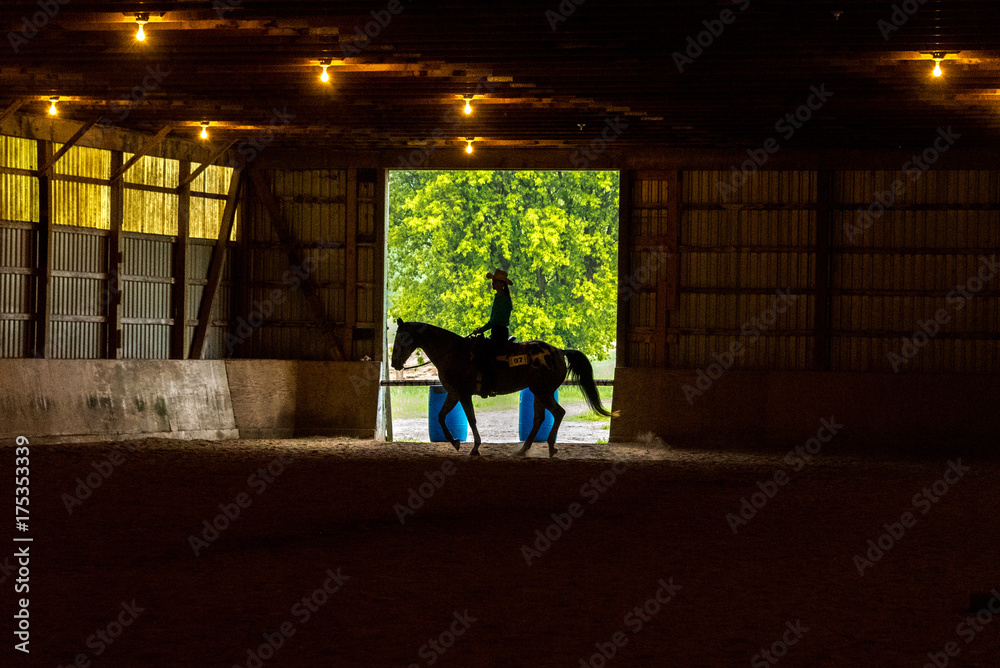 silhouette of cowgirl riding horse inside large barn