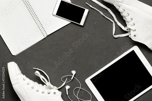 Stylish casual Flat lay Of White Sneakers On black Background with phone, headphones, tablet, copy book