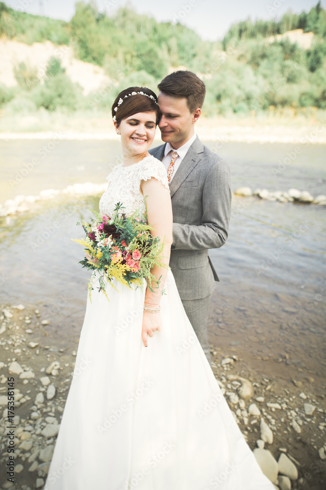 Bride and groom holding beautiful wedding bouquet. Posing near river Bride and groom holding beautiful wedding bouquet. Posing near river