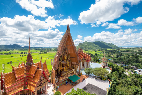 Above view of golden church with big buddha statue and rice field in Wat Tham Sua temple