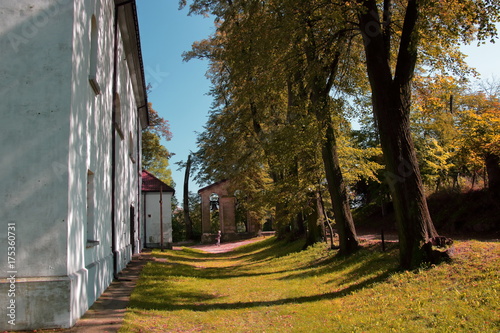 Jesienny pejzaż w Dobczycach, województwo małopolskie, Polska, drzewa w jesiennych kolorach rzucają cień na ziemię i ścianę kościoła