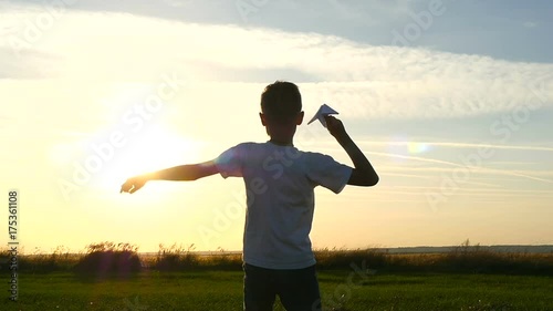 Happy guy playing with a paper airplane in a field in the sun. Silhouette at sunset photo