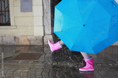 Person with pink boots and blue umbrella splashing in the puddle