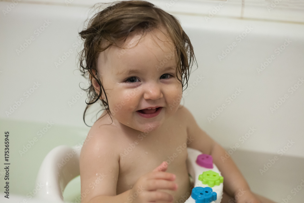 Blue eyes little girl in the bathing bucket looking at the camera and smiling. Happy baby having a bath and playing with rubber toys Blue eyes little girl in the bathing bucket looking at the camera and smiling. Happy baby having a bath and playing with rubber toys